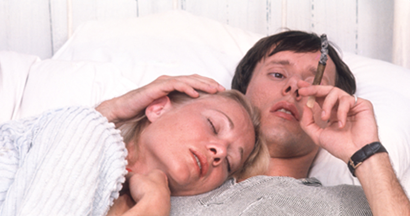 Image of a woman laying her head on a man while he smokes a cigar