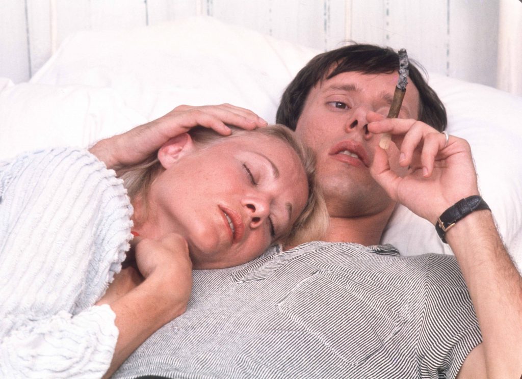 Image of a woman laying her head on a man while he smokes a cigar