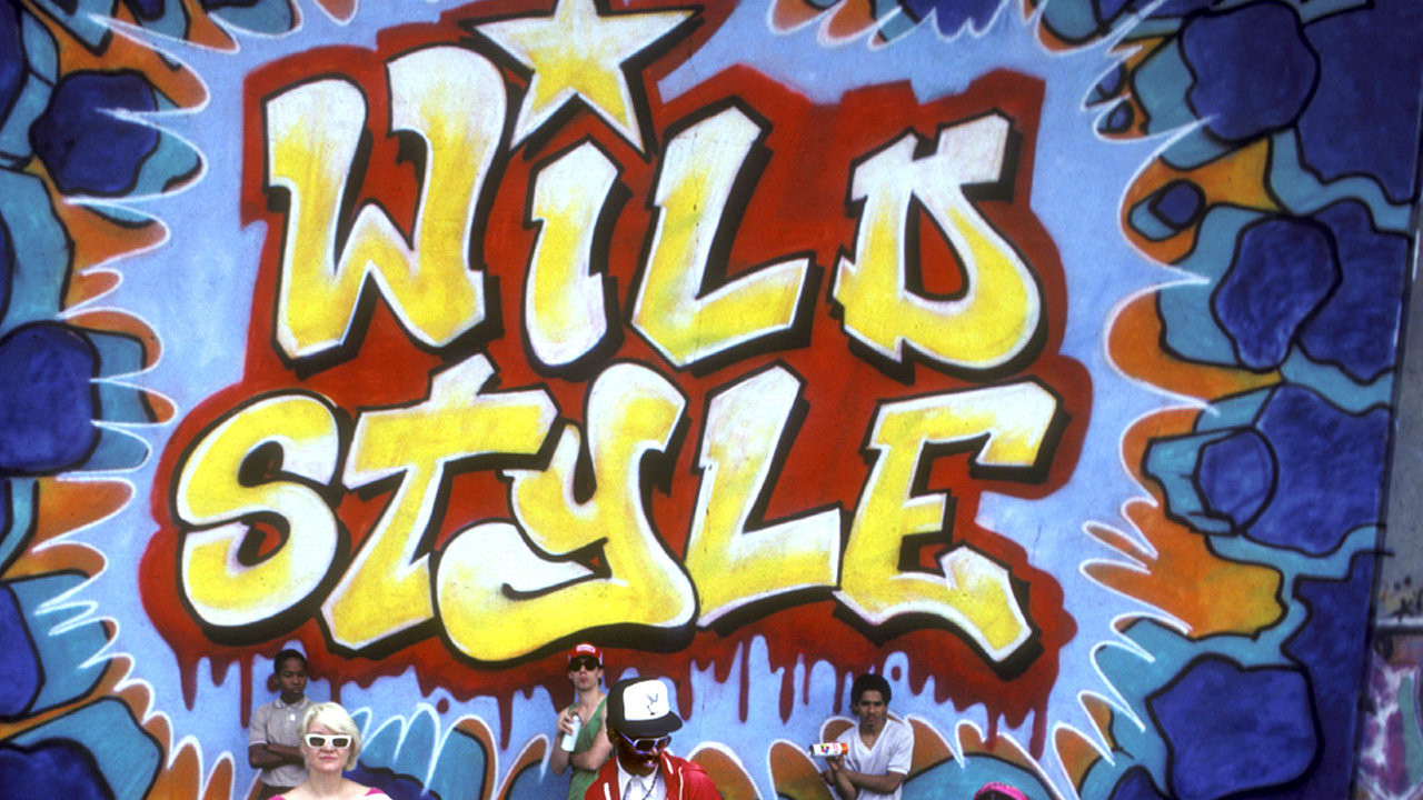 Image of people posing in front of a graffiti wall with the words "Wild Style"