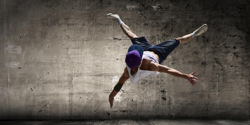 Male dancer in purple hat doing a flip in mid air