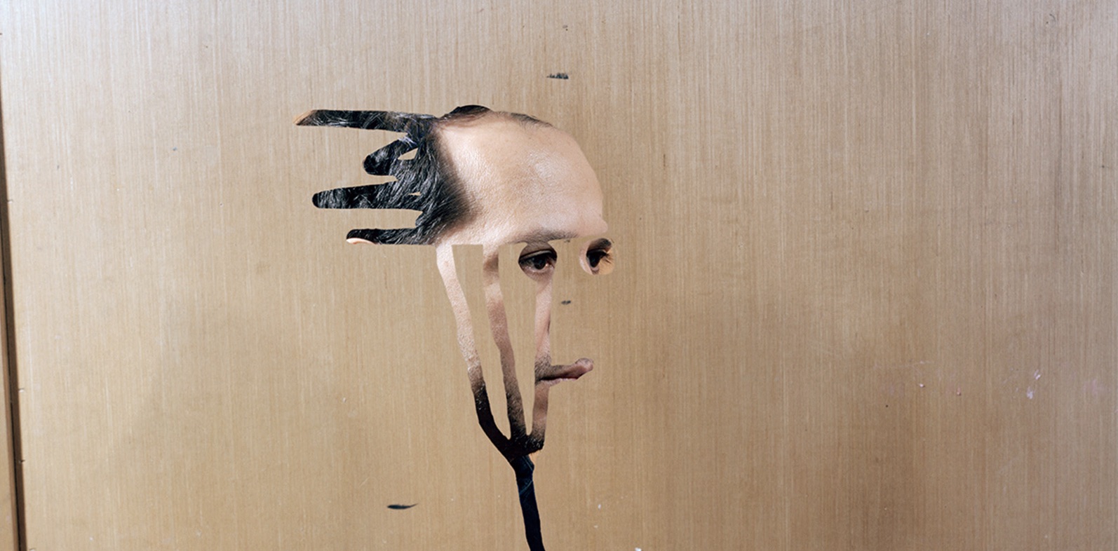 Man is seen through a carving in a door. The carving looks like a pitchfork with a wig atop it.