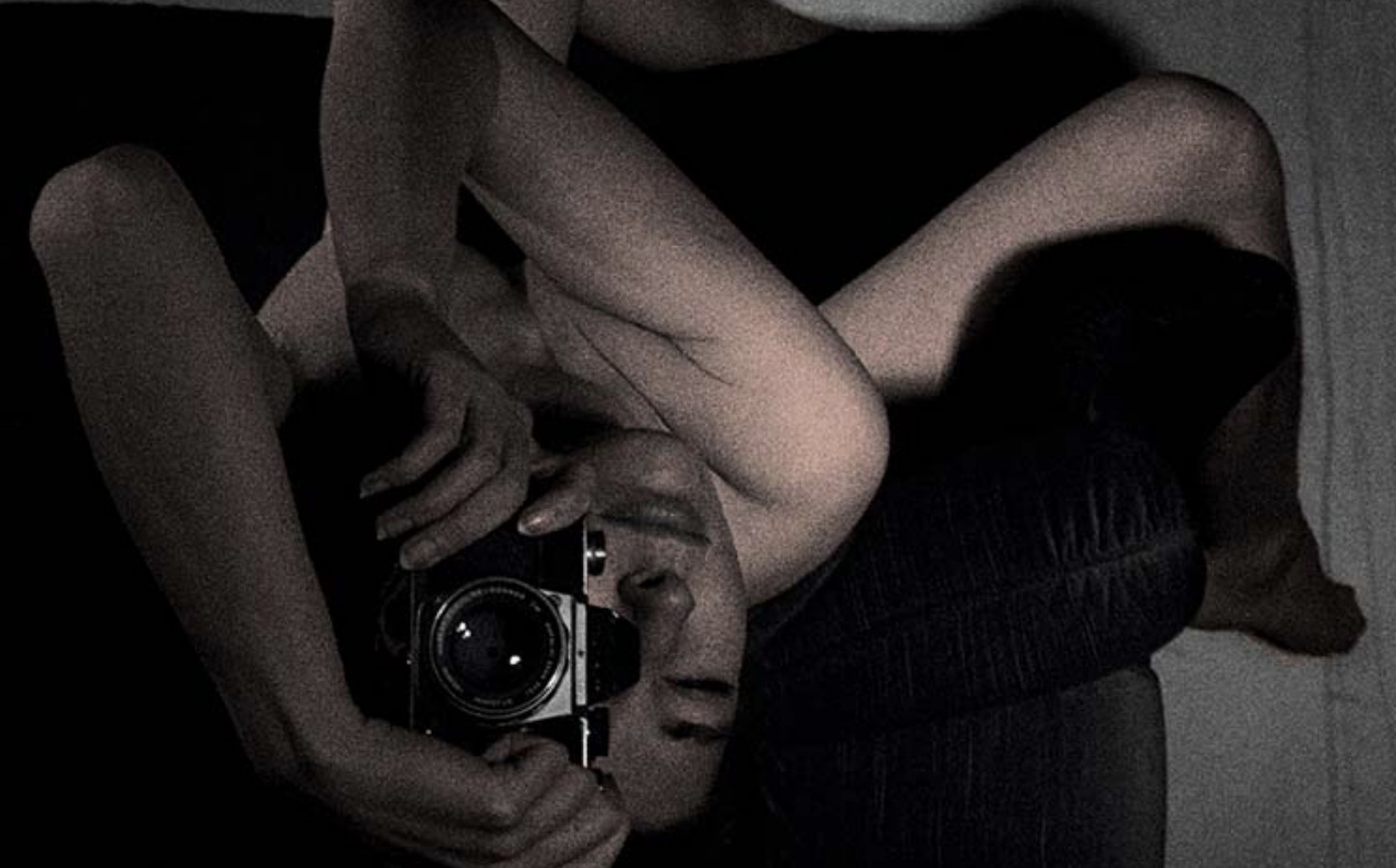 Naked photographer twisted upside down on a couch taking a photo