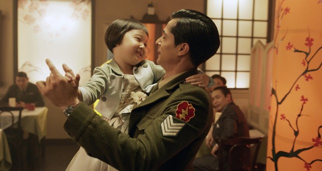 An Asian man in a green military uniform dances with a little girl in his arms. They look to be in a restaurant