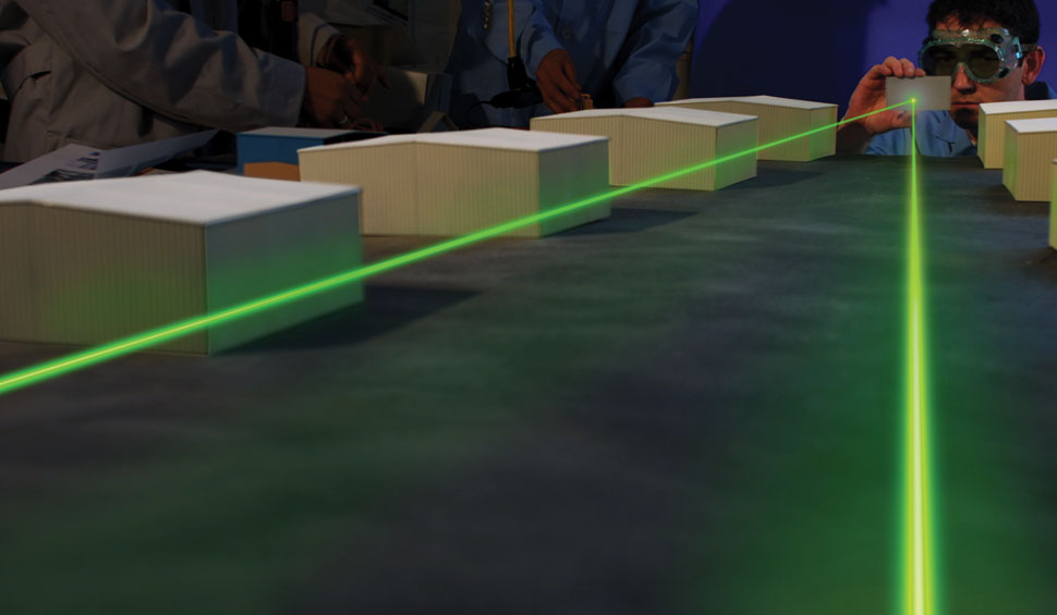 A scientist in protective goggles bounces a green laser off a mirror in two directions