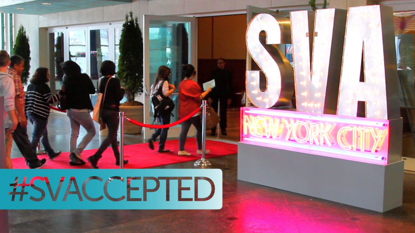 Students entering a building via a red carpet with red roped stanchions on either side. A large, lit up SVA New York City sculpture sits outside the entrance