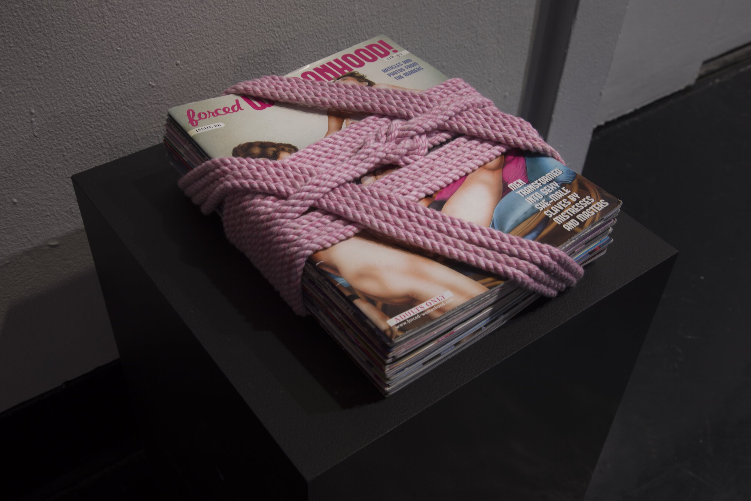 Image of a stack of "forced Womanhood!" magazines bound by heavy rope