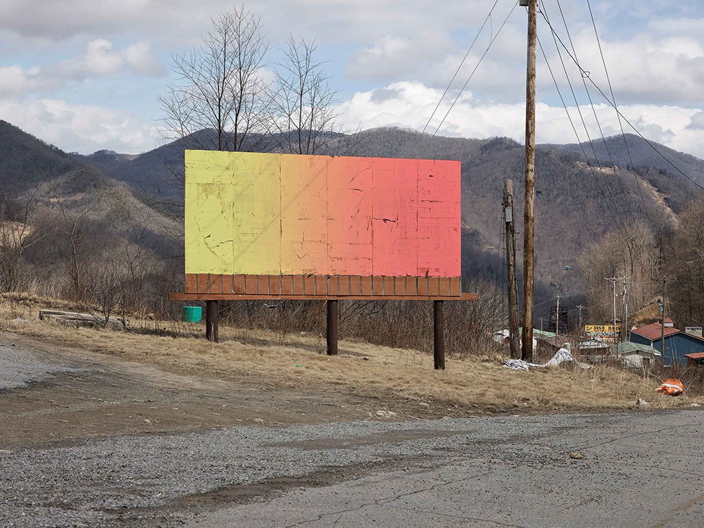 Image of billboard on the side of the road painted yellow, orange and red.