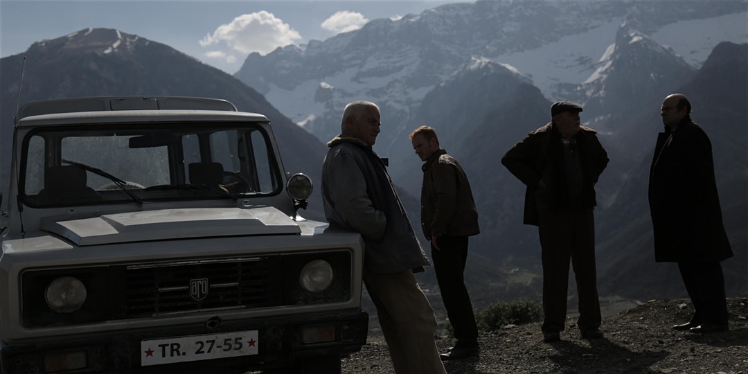 Four men standing next to a car in the mountains