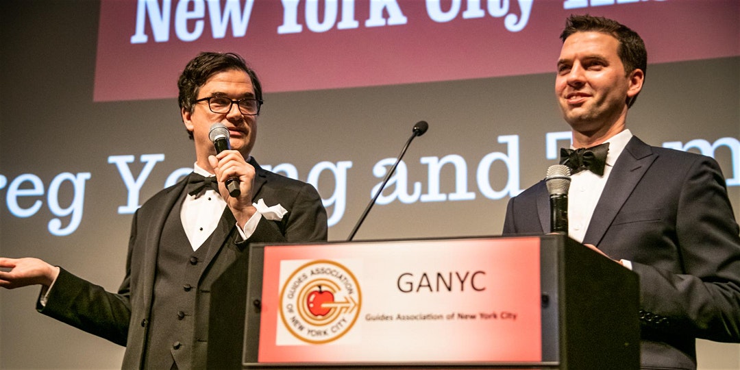 Two men in tuxedos speaking behind a podium at the GANYC Awards
