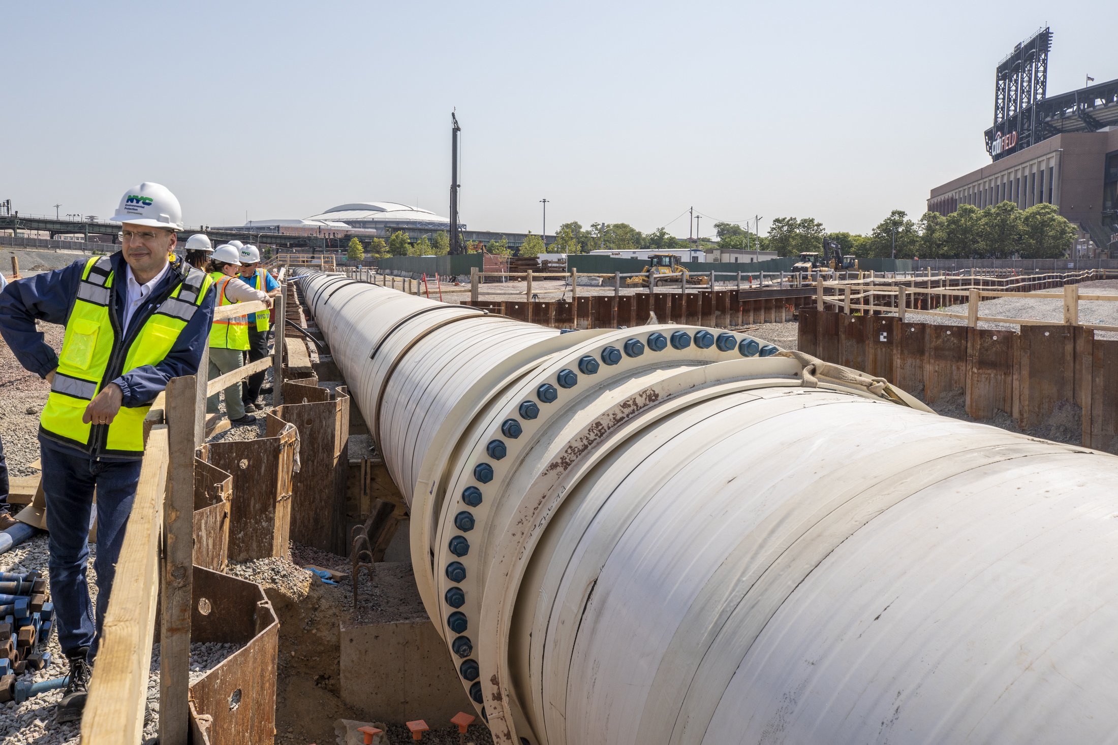 Person with a construction vest leaning near an industrial pipe near Citi Field.