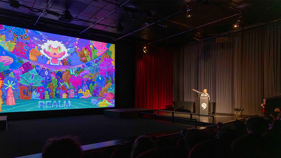 A person points to an animated image shown on screen in a theater.