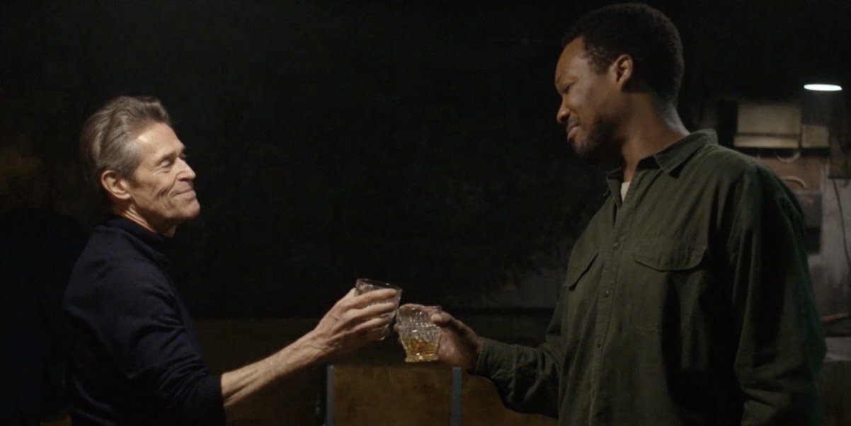 Willem Dafoe and Corey Hawkins clinking glasses of whiskey. Image from the film "The Man in My Basement"