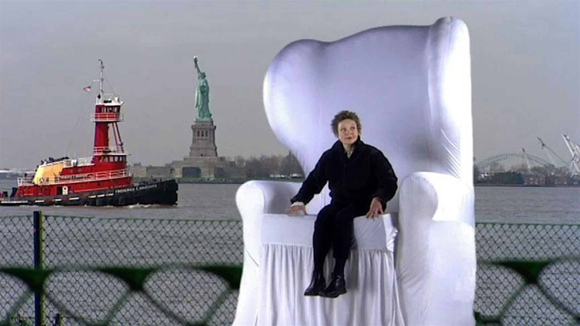 Women sitting in large white chair with Statue liberty in the background